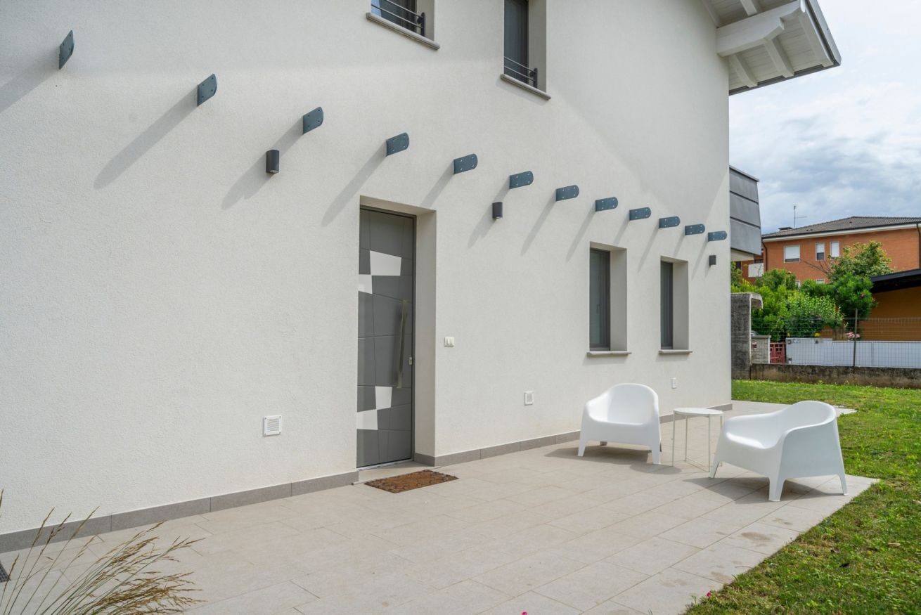 A modern building with a white exterior, a door, and a small patio area with two white chairs and a table.