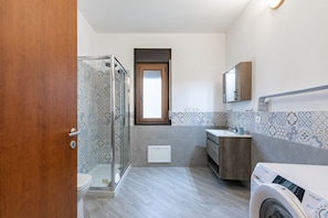 A bathroom with a shower, toilet, sink, and washing machine.