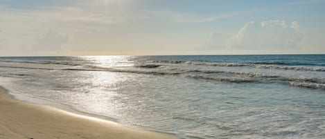 Uma praia com pegadas na areia e ondas se aproximando da costa.