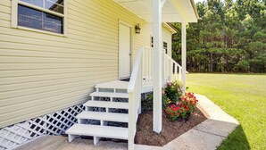 Keltainen talo, jossa on valkoinen kuisti, portaat ja pieni puutarha, jossa kasvaa punaisia kukkia.