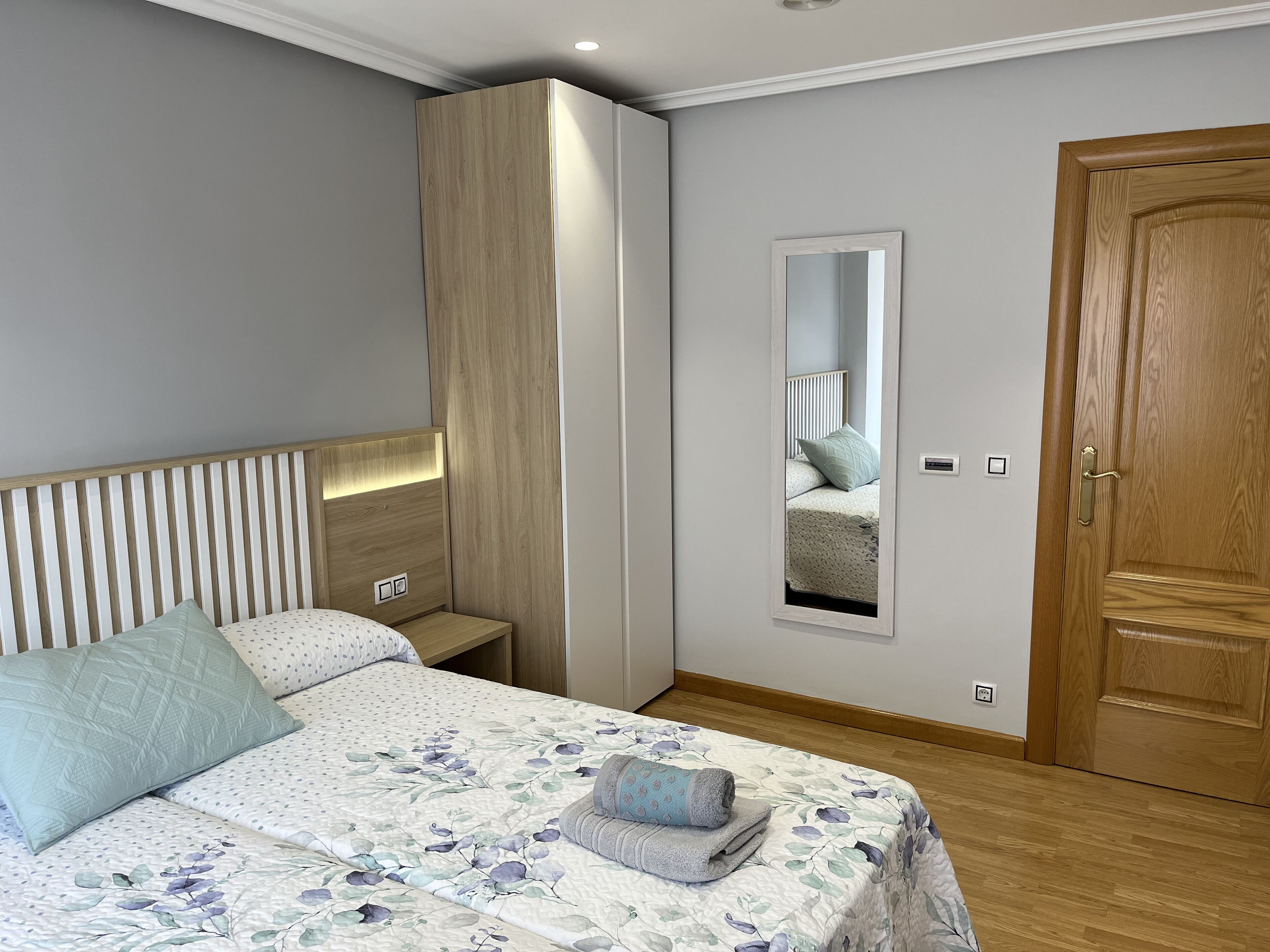 Een slaapkamer met een bed, een kledingkast, een spiegel en een deur.