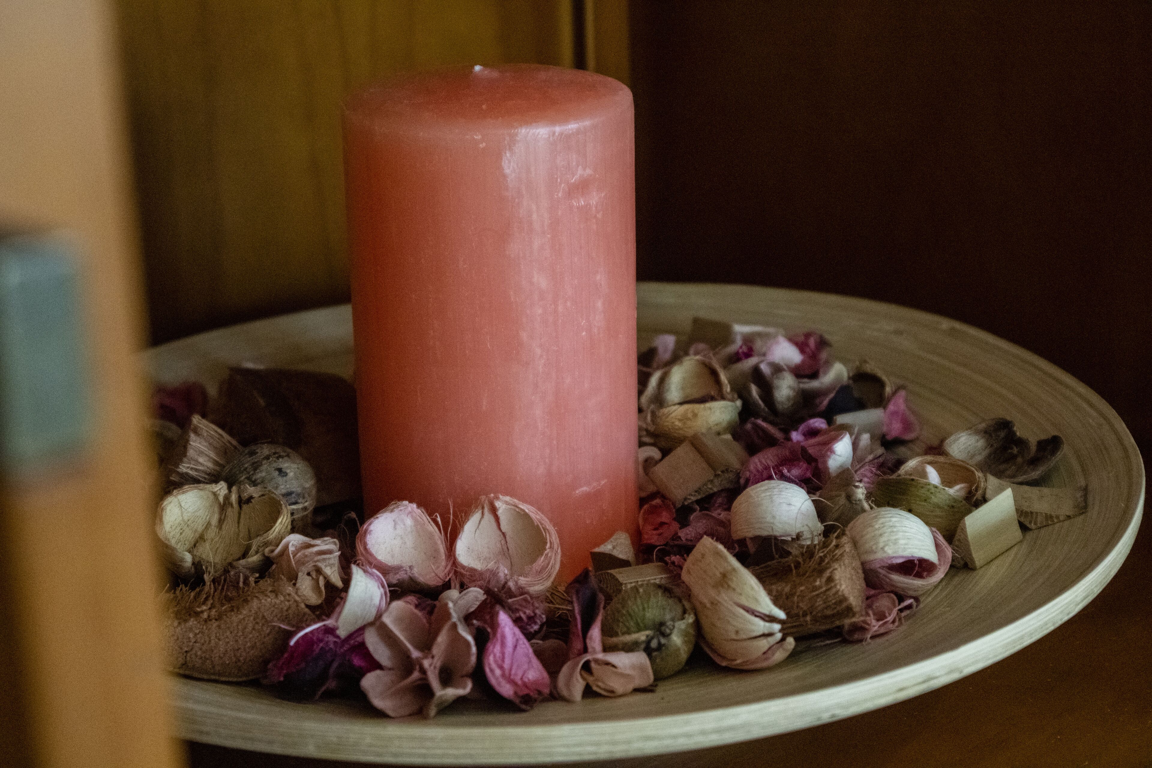 A large candle on a plate surrounded by dried flowers and herbs.