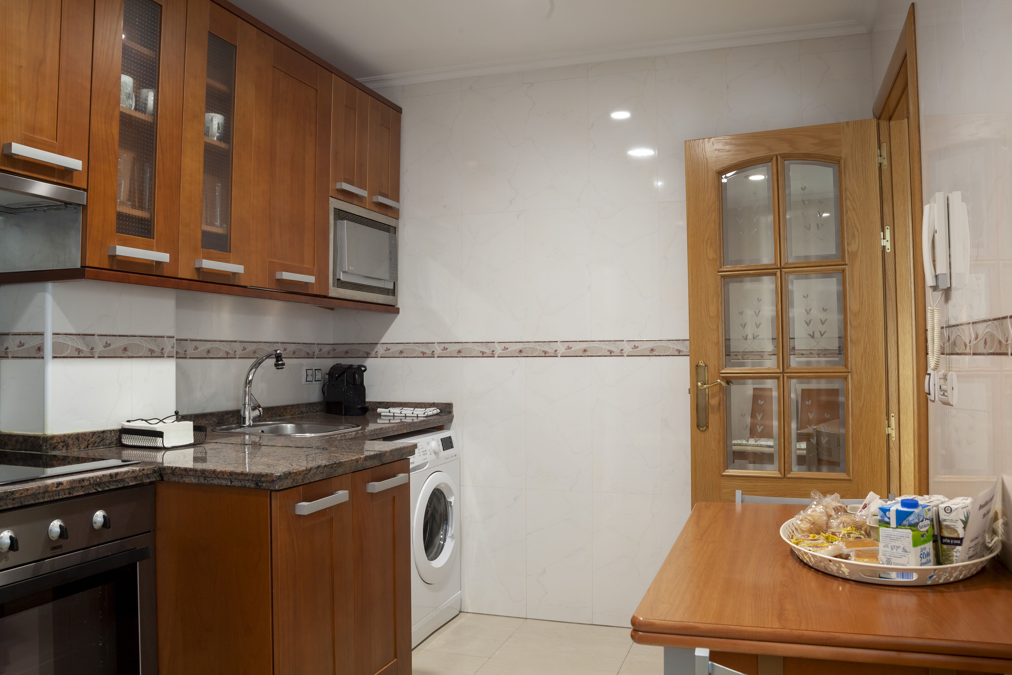 A kitchen with wooden cabinets, a microwave, a washing machine, and a dining area with a table.