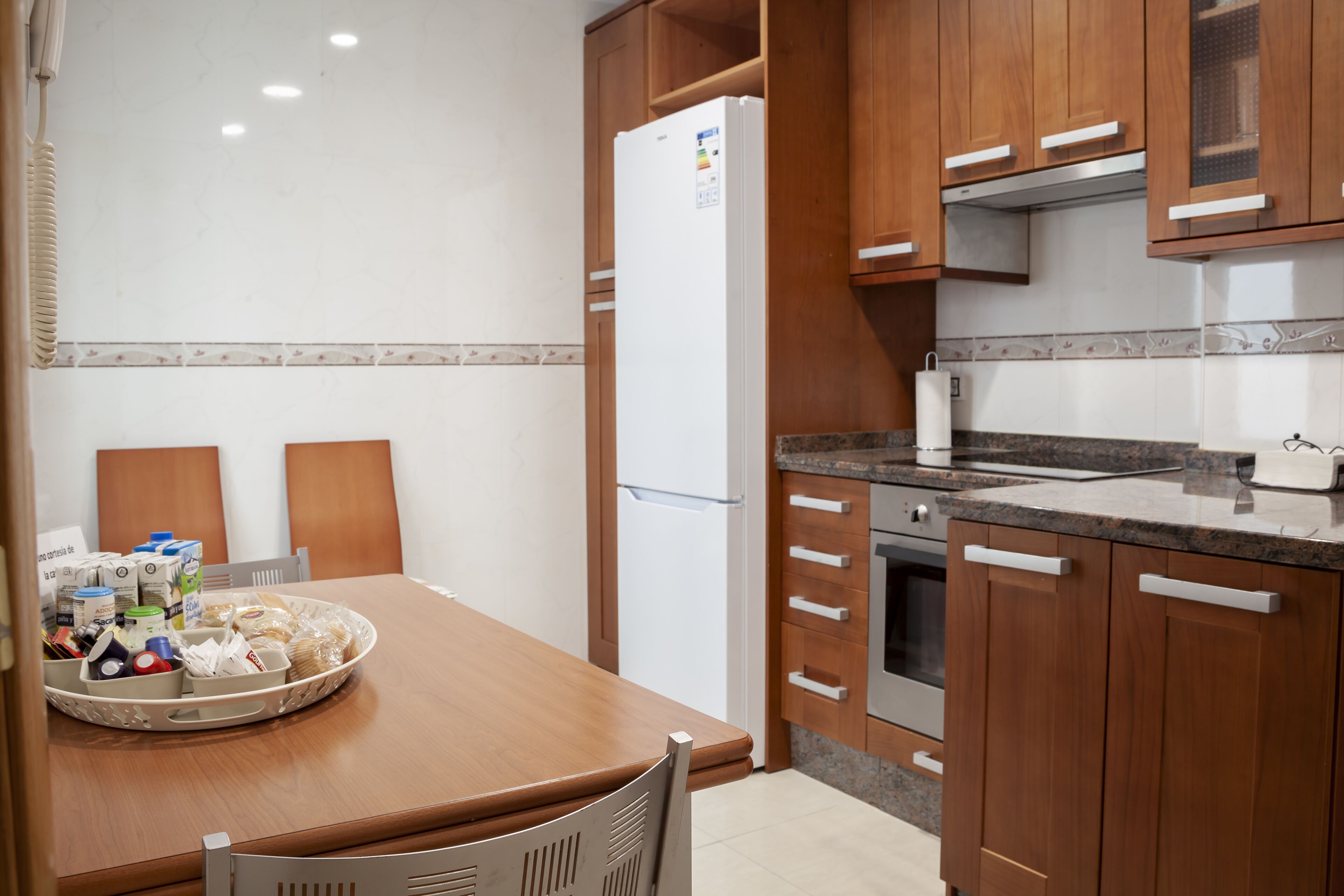 A kitchen with wooden cabinets, a refrigerator, and a dining table with chairs.