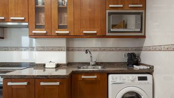 Una cocina con armarios de madera, un microondas, un lavabo y una lavadora.