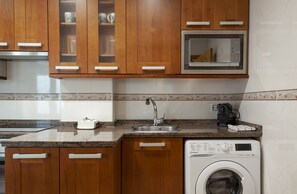 Una cocina con armarios de madera, un microondas, un lavabo y una lavadora.