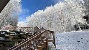 Een houten trap leidt naar een stenen muur, omgeven door met sneeuw bedekte bomen en een heldere blauwe lucht.
