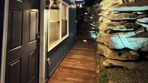 Een huis met een donkere voordeur, een houten looppad en een stenen muur met een waterval.