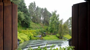 Vista a través de una ventana de madera de un jardín exuberante con césped verde, árboles y un pabellón.