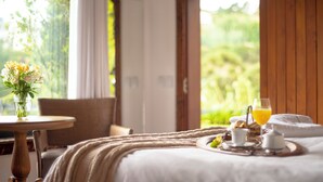 Un dormitorio con cama, una mesita de noche con un florero y un vaso de jugo de naranja, y una bandeja con alimentos para el desayuno.