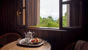 Una mesa de comedor con una bandeja de fruta y una tetera, frente a una ventana con vistas a la vegetación.