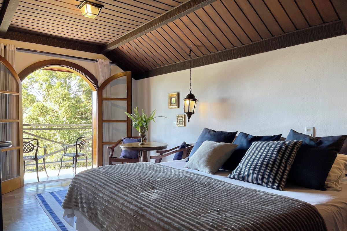 Un dormitorio con una cama grande, un balcón con sillas y vistas a árboles.