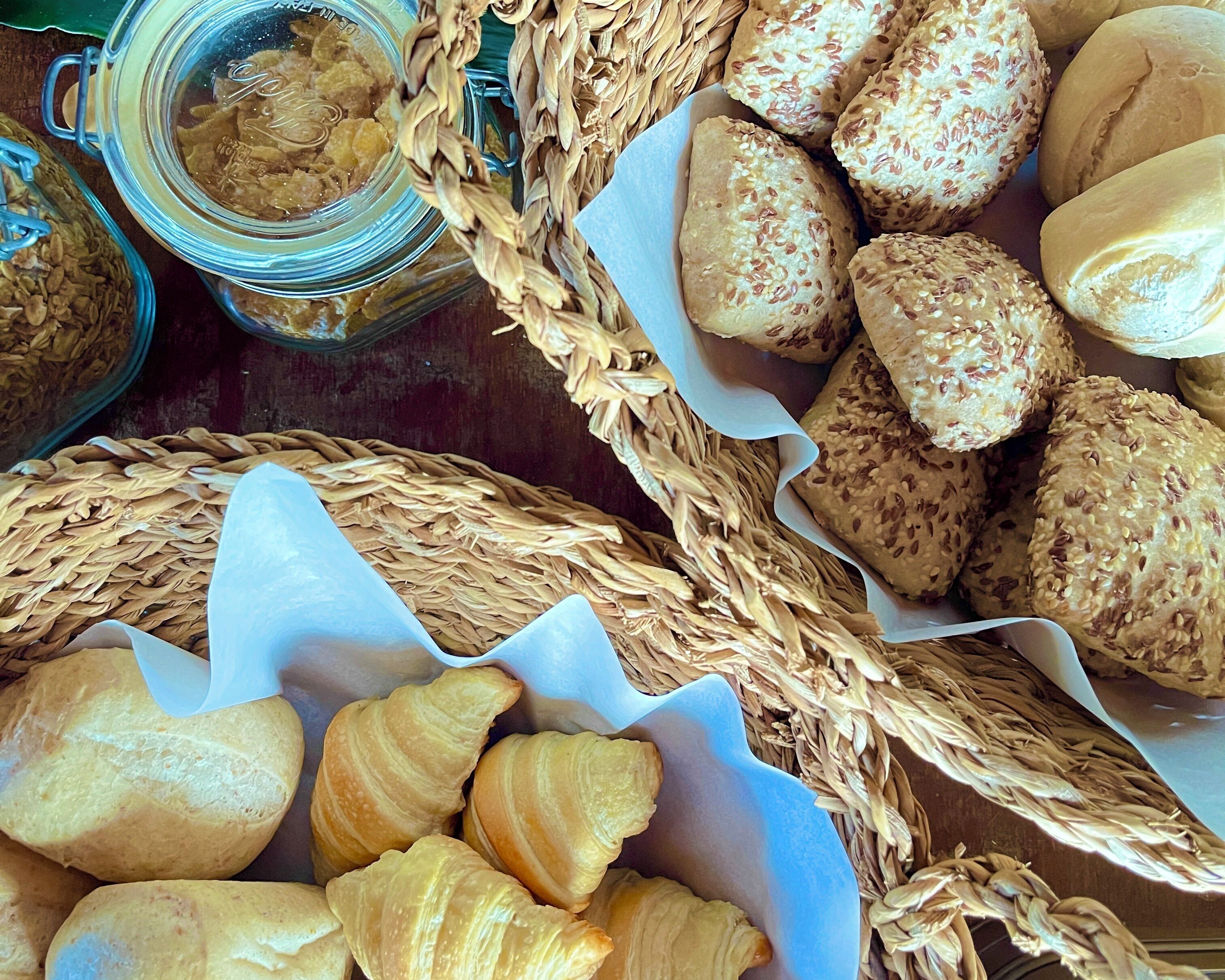 Verschiedene Backwaren, darunter Brot, Croissants und Gebäck, präsentiert in Körben und auf einer Tischplatte.