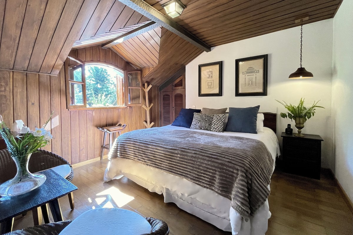 Un dormitorio acogedor con una cama grande, techo de madera y ventana con vistas a zonas verdes.