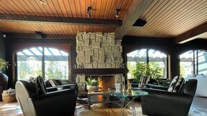 Una sala de estar acogedora con sofás de cuero, una mesa de centro de vidrio, una chimenea de piedra y ventanas amplias.