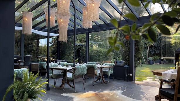 Un área de comedor al aire libre cubierta con mobiliario de mimbre, luces colgantes y un tapete de cuero de vaca.