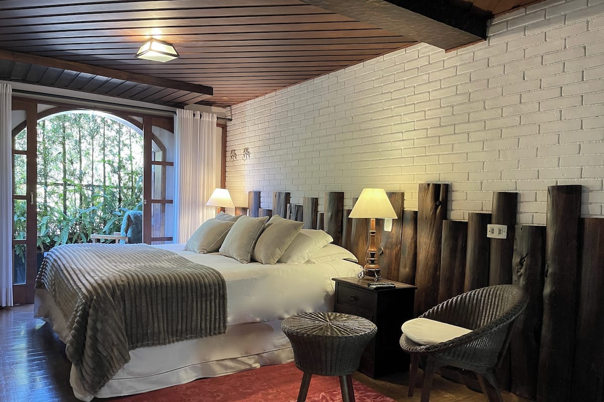 Un dormitorio con una cama, dos lámparas de noche, una silla de mimbre, una mesita de noche y una alfombra roja.