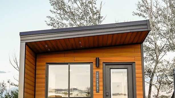 A modern cabin with a wooden exterior, a large window, and two Adirondack chairs outside. - The Fremont - Studio Tiny Home (Wayne County)