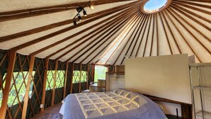 Interior de una yurta con una cama, una mesita y una ventana.