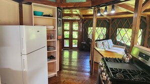 Una cocina de estilo rústico tipo cabaña, con vigas de madera, un refrigerador blanco, una estufa y un ventanal grande.