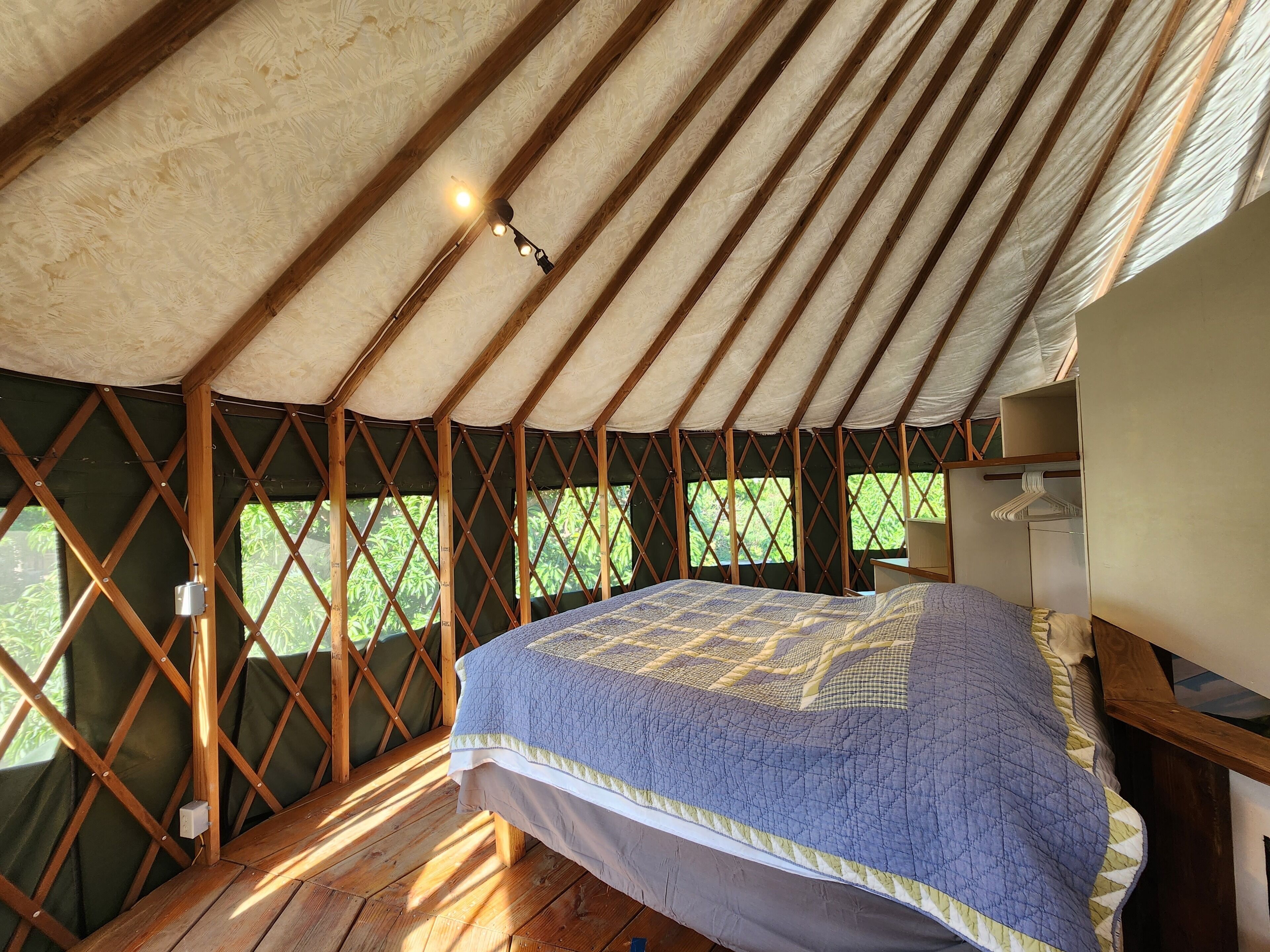 A cozy tent with a bed, wooden beams, and a view of greenery outside.