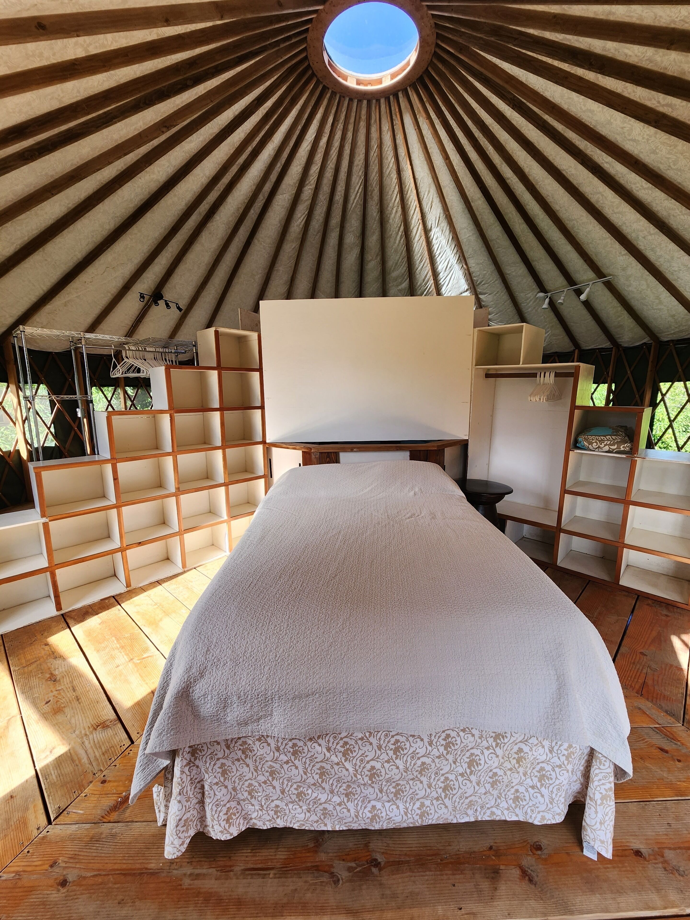 A tent with a bed, wooden shelves, and a circular skylight.