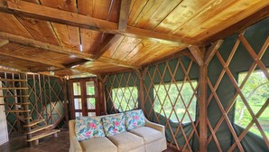 Un interior acogedor con techo de madera, un sofá con cojines florales y vistas a través de una ventana con celosía.