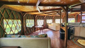 Una cabaña acogedora y rústica con interior de madera, un sofá, una mesita y una zona de cocina con estufa.