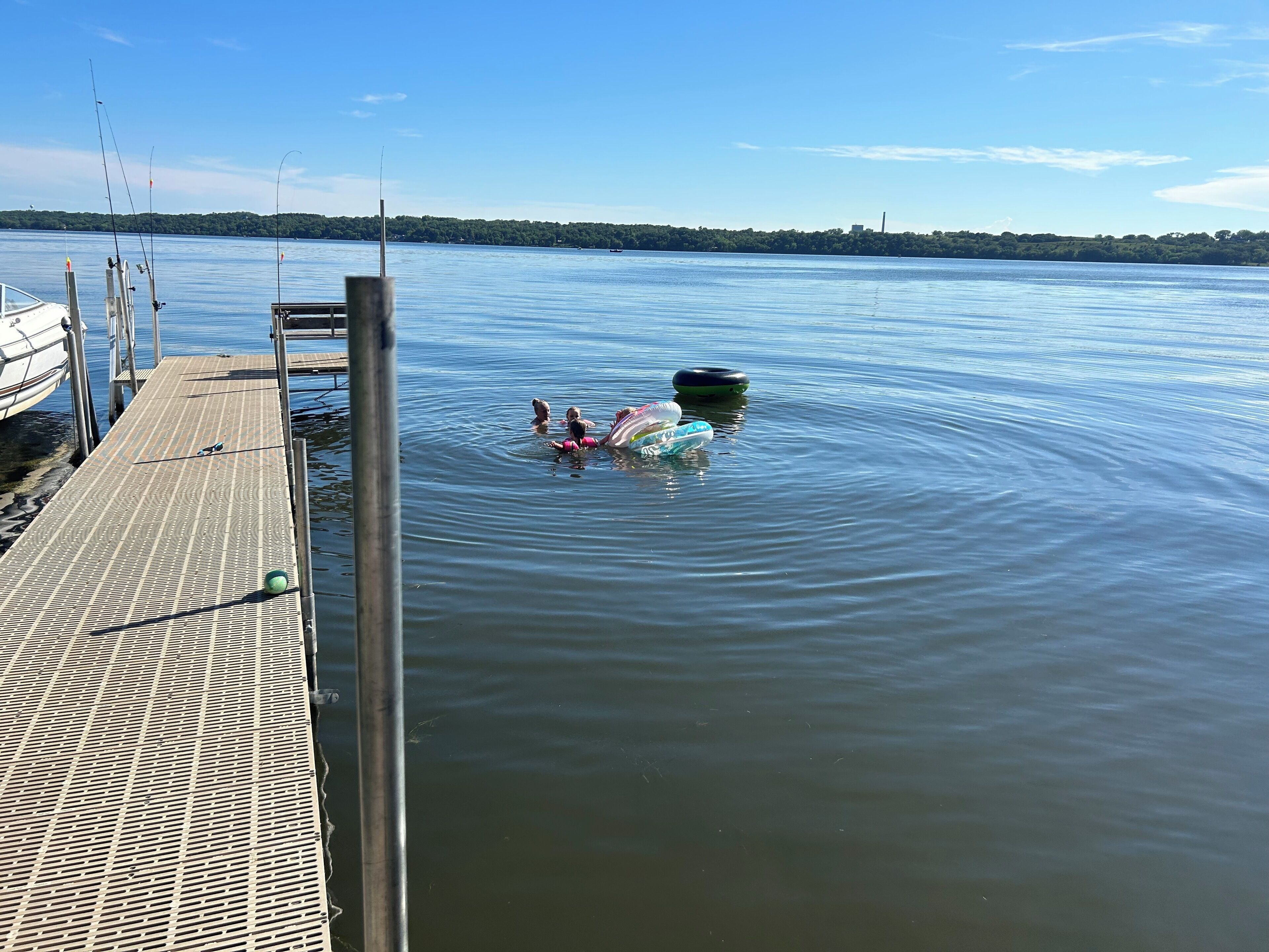 Een houten steiger die uitloopt in kalm water, met visstokken en een boot aan de linkerkant.