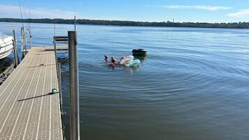 Een houten steiger die uitloopt in kalm water, met visstokken en een boot aan de linkerkant.