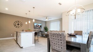 A modern kitchen with a central island, pendant lighting, and a dining area with a wooden table and chairs. - Gorgeus HOUSE Near Disney & FREE water park 4963 (Kissimmee)
