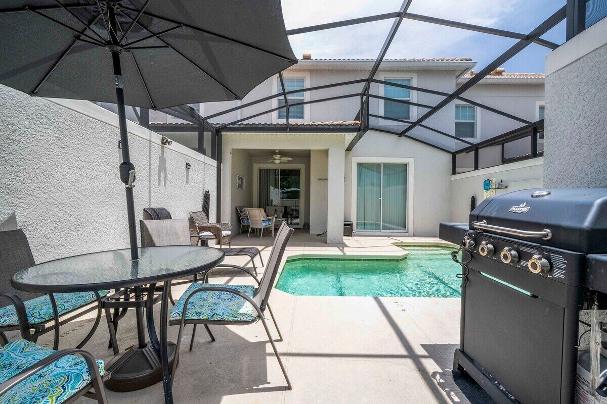 Un patio con piscina, una parrilla y mobiliario exterior.