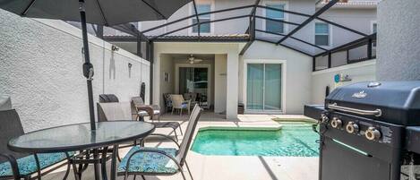 Un patio con piscina, una parrilla y mobiliario exterior.