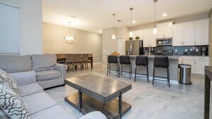 A modern living room with a sofa, a coffee table, and a dining area with chairs and a table. - Gorgeus HOUSE Near Disney & FREE water park 4963 (Kissimmee)