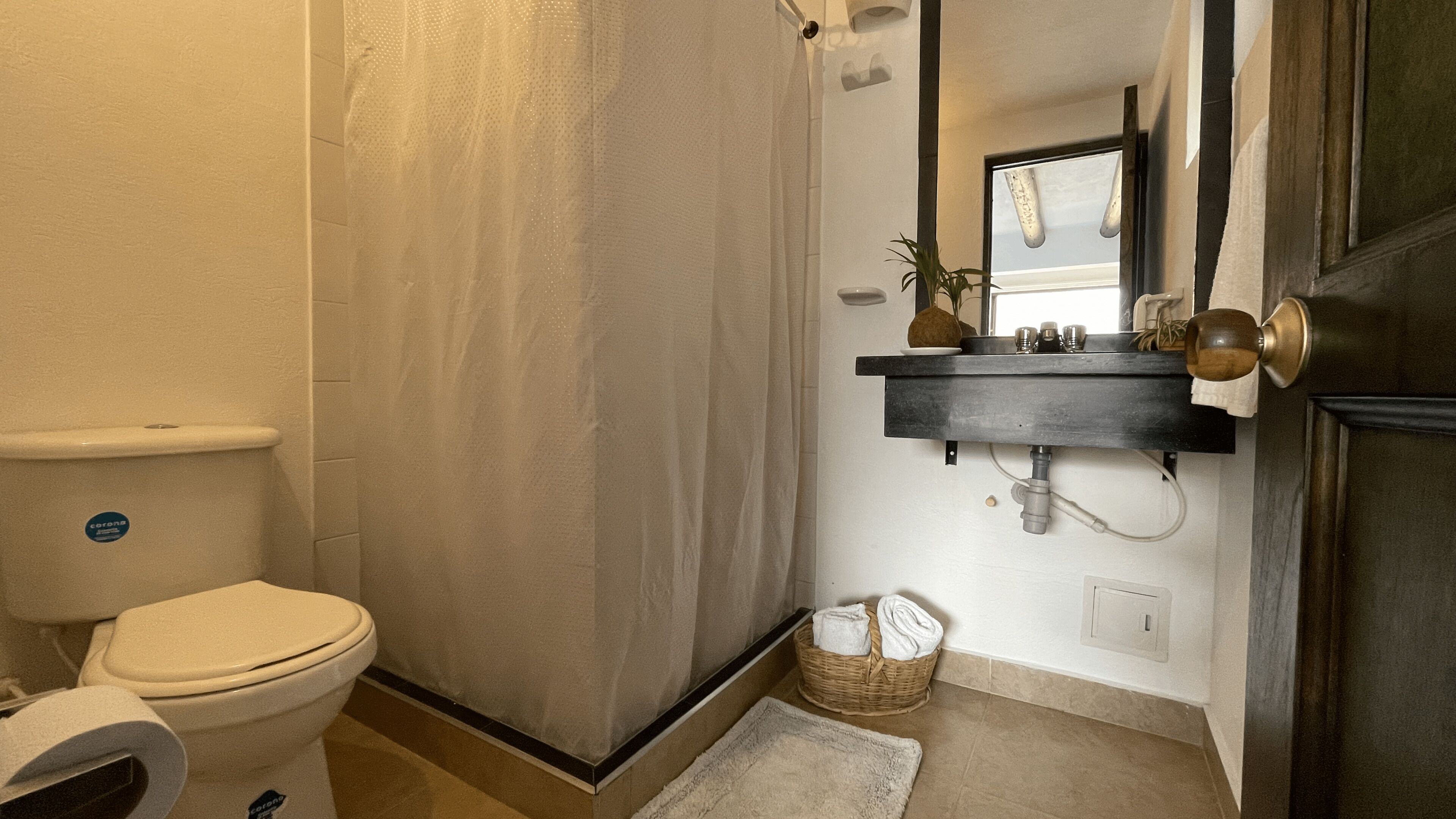 A bathroom with a toilet, shower curtain, sink, and a small basket on the floor.