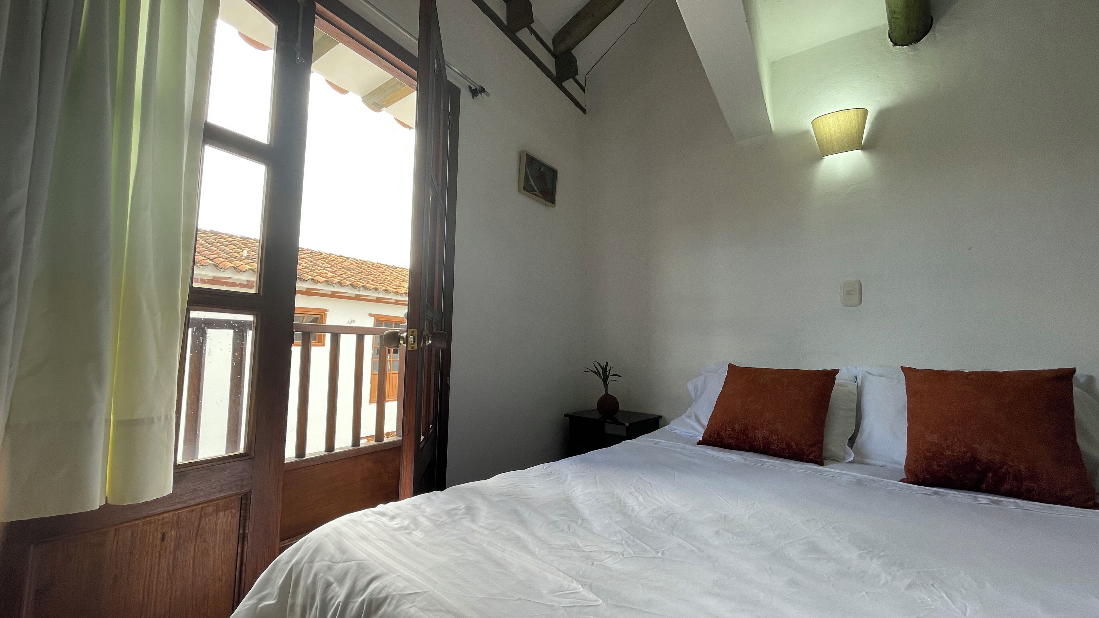 Une chambre à coucher avec un lit, une table de chevet, une lampe fixée au mur et une fenêtre avec des rideaux.