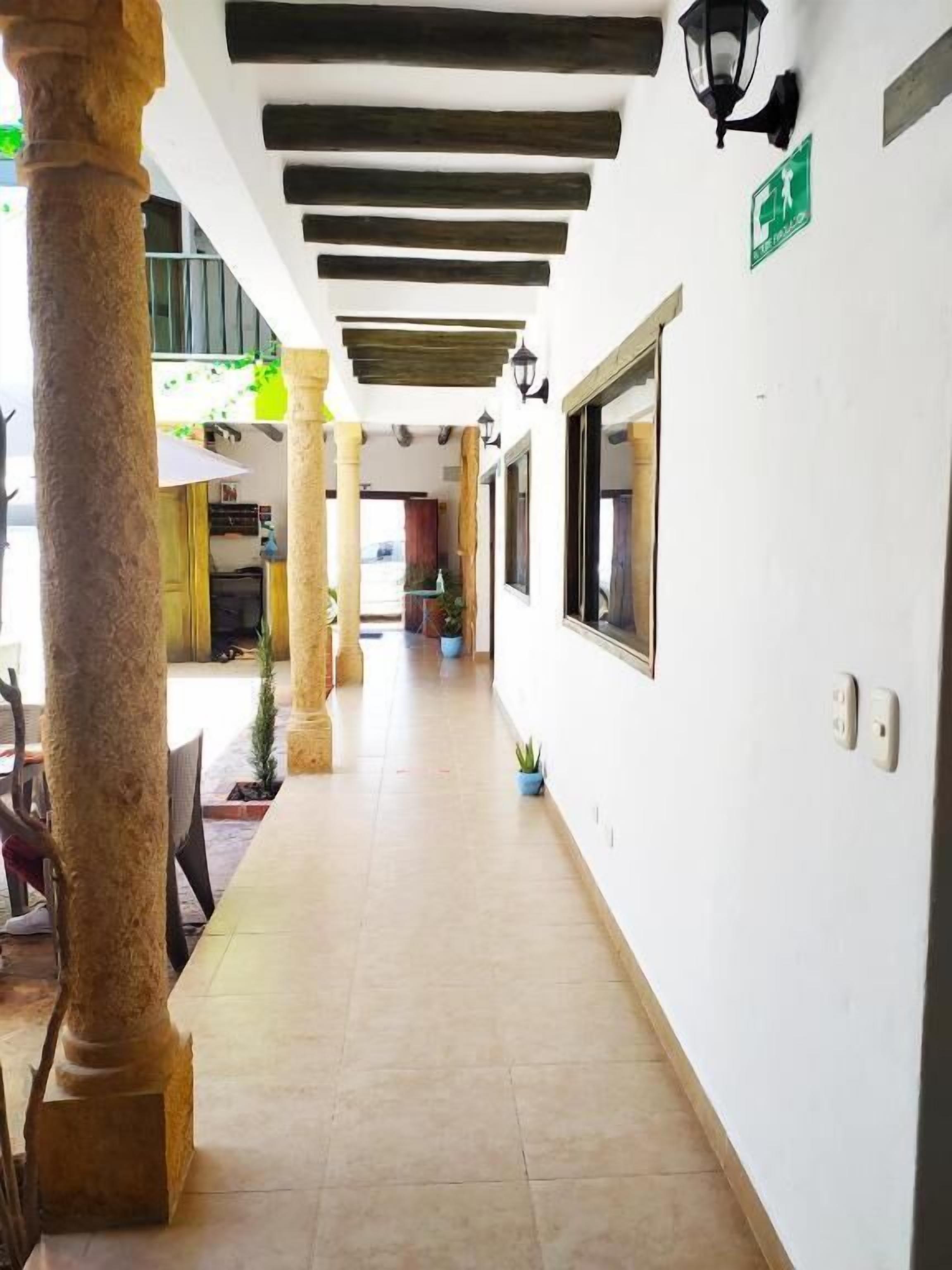 Un pasillo con suelo de baldosas, vigas de madera en el techo y un letrero de salida verde.