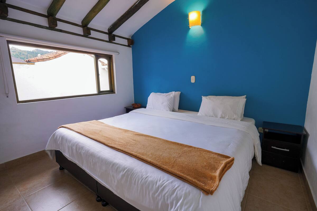 Ein Schlafzimmer mit Bett, Fenster, Nachttisch und einer wandmontierten Lampe.