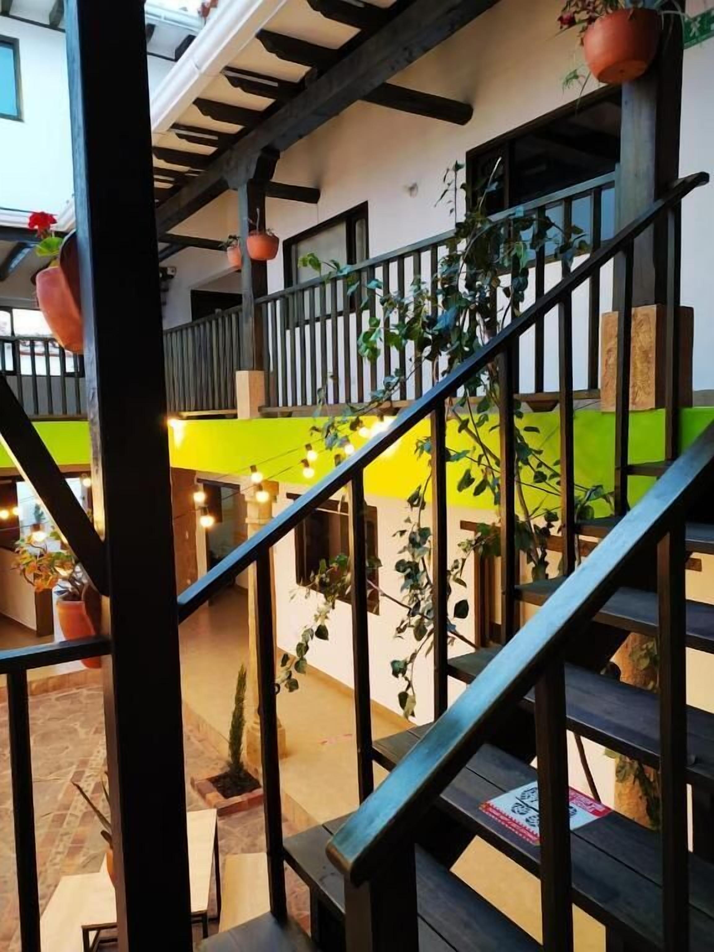 Un espace extérieur à plusieurs niveaux, agrémenté d’escaliers en bois, de plantes en pot et d’un mur jaune vif.