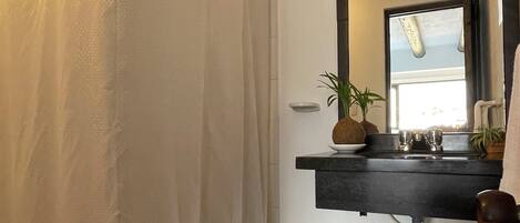 A bathroom with a shower curtain, a sink with a mirror, a small plant, and a basket with towels.