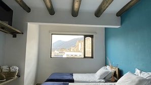 Un dormitorio con dos camas, una ventana con vistas a edificios y vigas de madera a la vista en el techo.