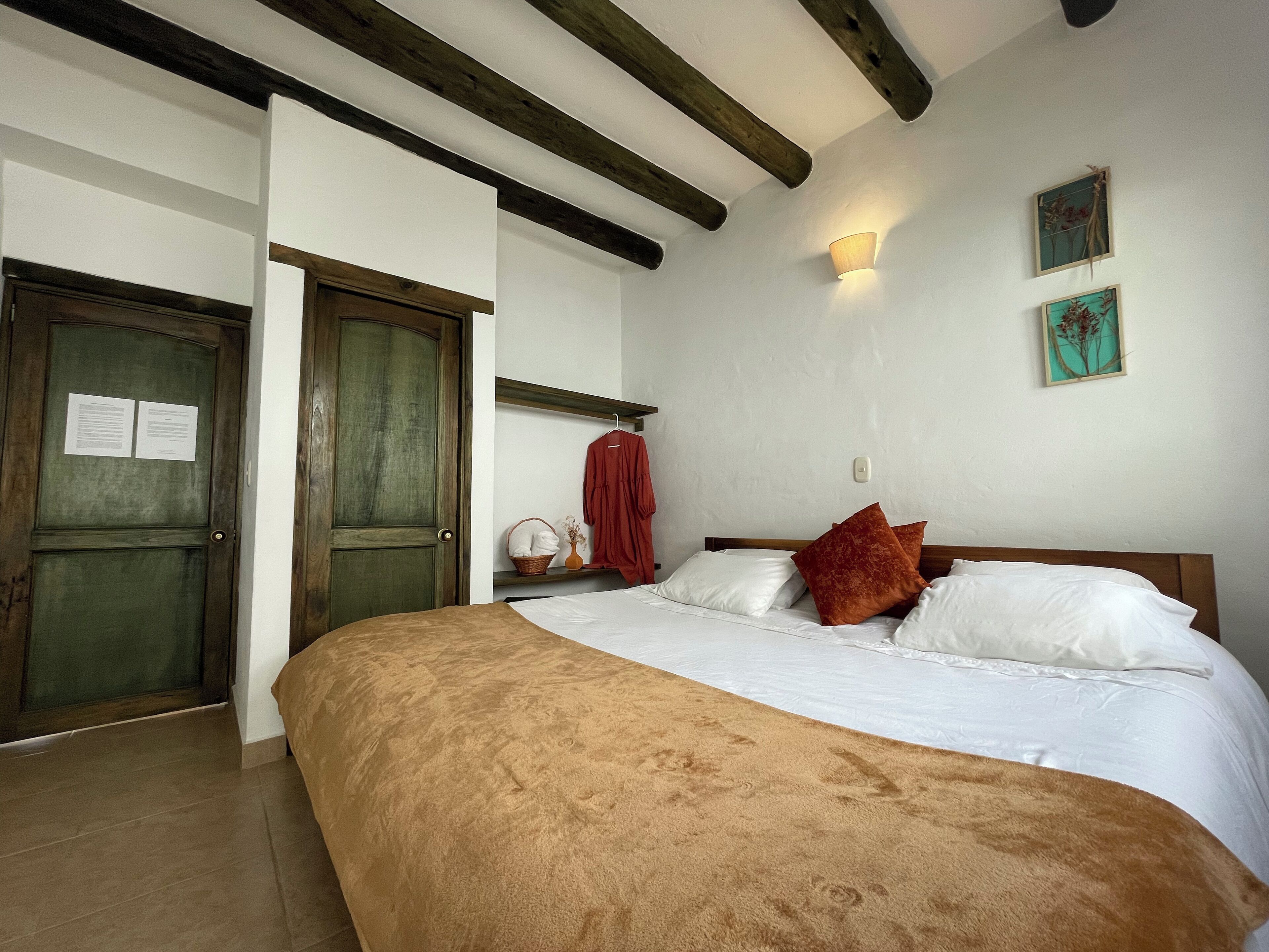 A bedroom with a large bed, wooden beams on the ceiling, a wall-mounted light, and a door with papers on it.
