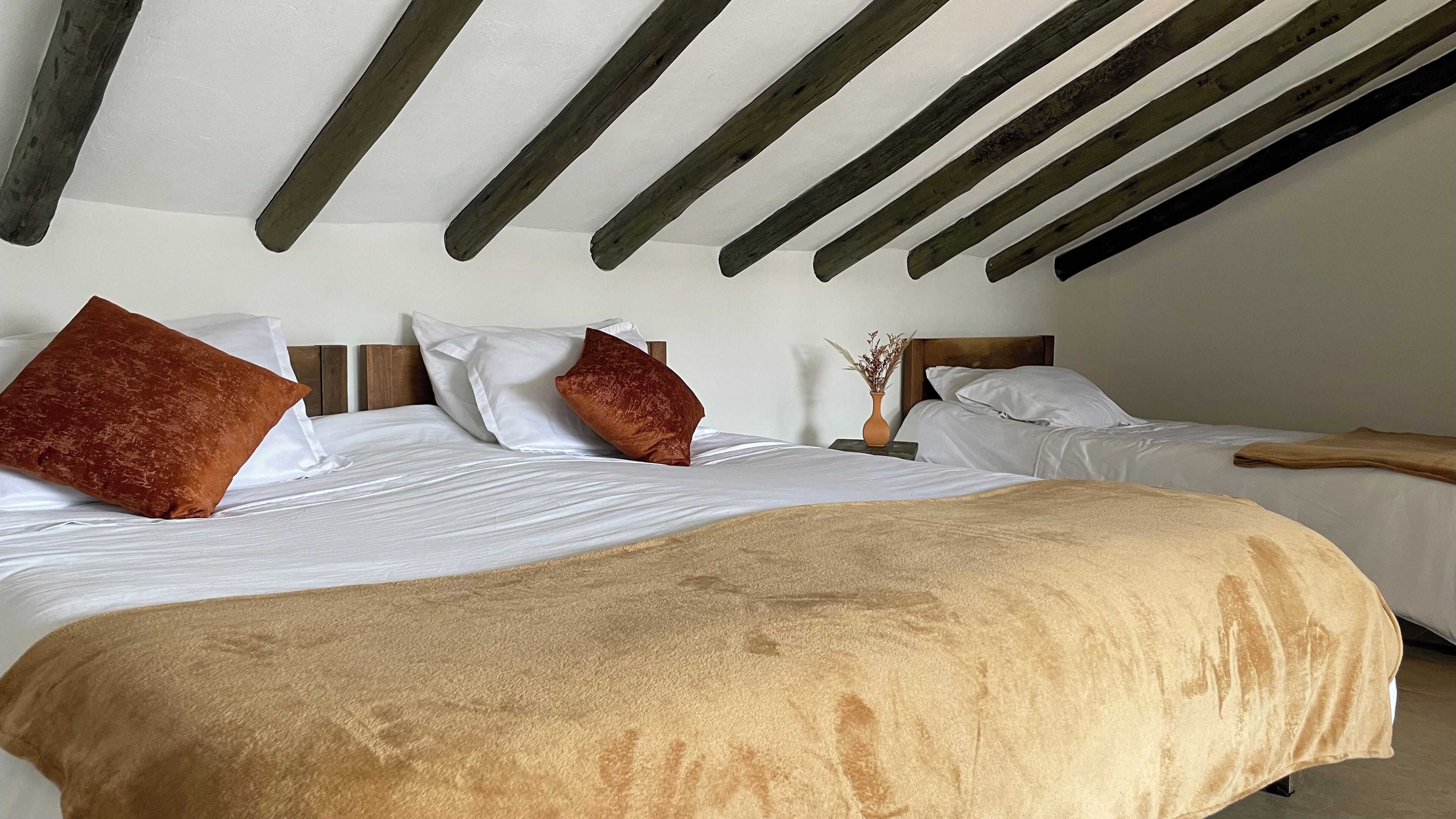 Un dormitorio con dos camas, vigas de madera en el techo y un florero con flores secas en la mesita de noche.