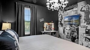 A bedroom with a bed, a chandelier, a window with curtains, and a wall with posters. - Swift BnB - Taylor themed rooms - Pool - sleeps 16 (Kissimmee)