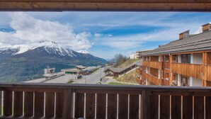 Un balcón de madera con vistas a una montaña y una carretera, con edificios al fondo.