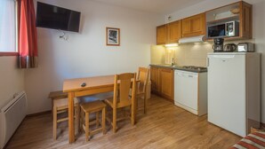 A compact kitchen with wooden cabinets, a microwave, a dishwasher, and a dining area with a table and chairs.