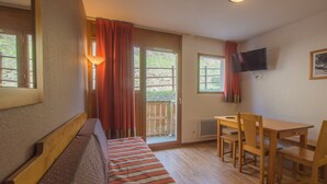 A room with a wooden bench, a table with chairs, a TV mounted on the wall, and a window with curtains.
