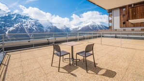 Una terraza con dos sillas y una mesa, con vistas a montañas nevadas bajo un cielo despejado.