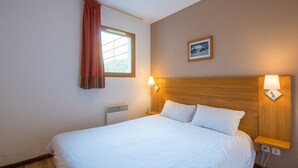 A hotel room with a large bed, a window with curtains, a wall-mounted picture, and bedside lamps. - Près du centre & des pistes | Charmant T3 de 55m² (Orcières)