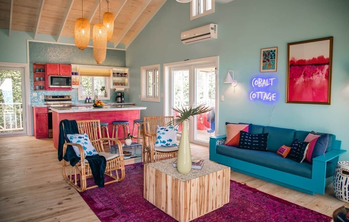A cozy living area with a sofa, chairs, a coffee table, and a kitchen in the background.